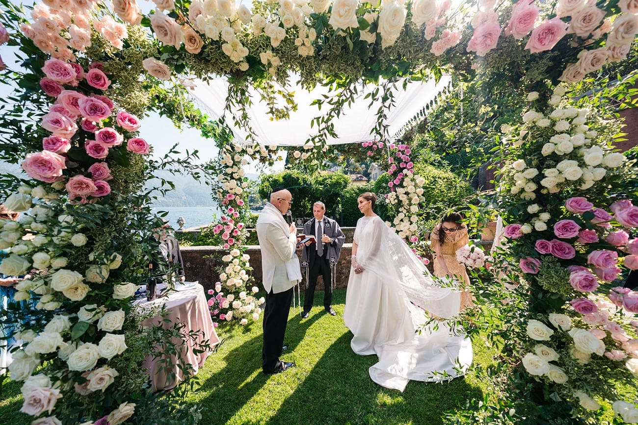 Bride and groom under flower arch - Join Us